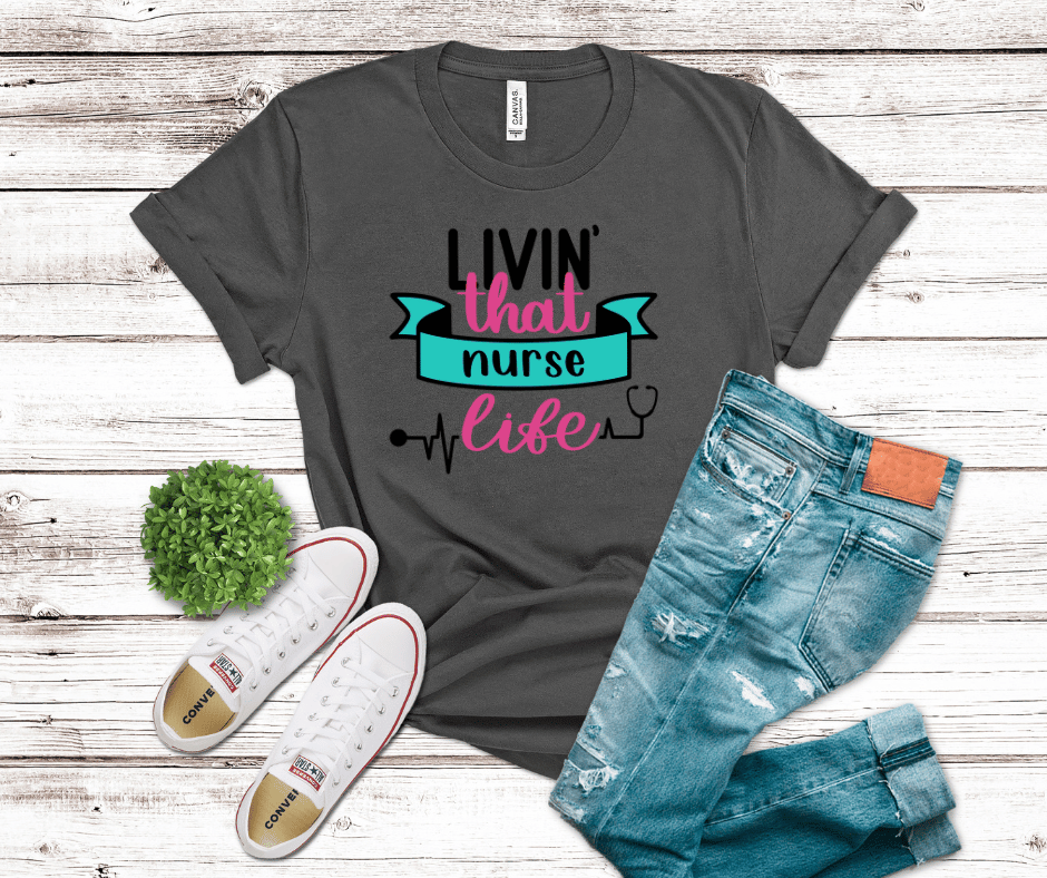 “Livin’ That Nurse Life” nurse graphic shirt with heartbeat line and stethoscope design on dark gray fabric.
