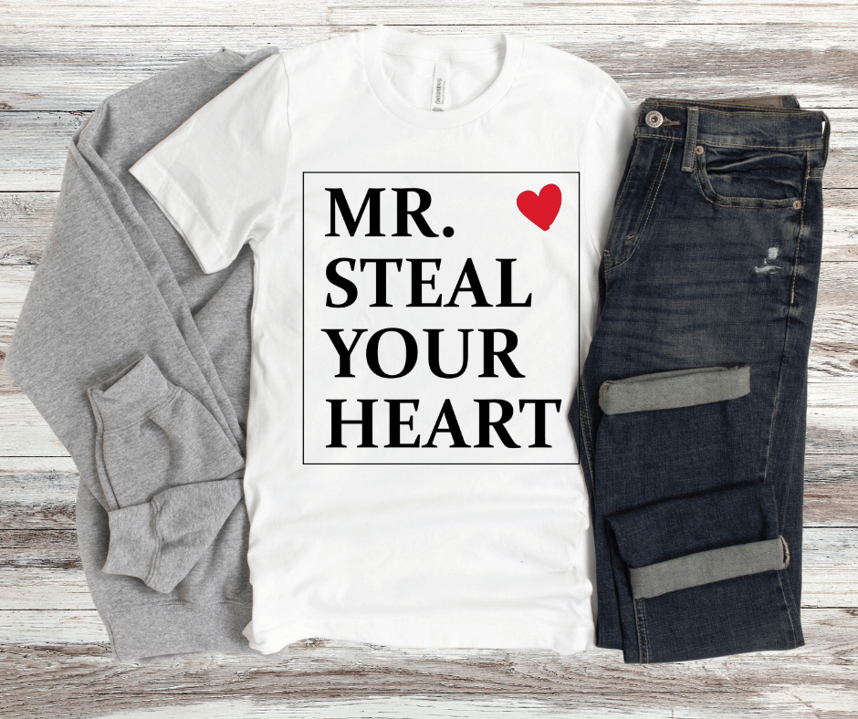 “Mr. Steal Your Heart” graphic shirt with bold black text and red heart detail on white fabric.