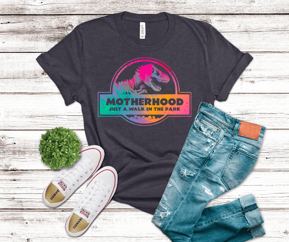 Rainbow dinosaur DTF transfer featuring a T-rex silhouette and the phrase “Motherhood Just a Walk in the Park” in a retro badge style with vibrant colors.