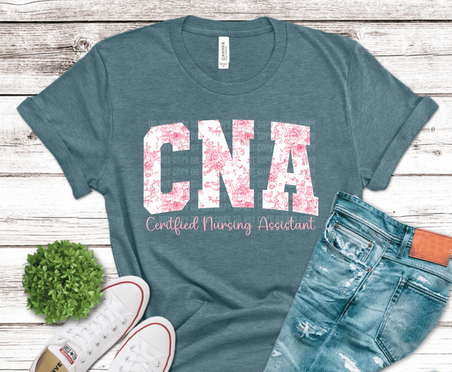 Teal t-shirt with 'CNA Certified Nursing Assistant' text on a wooden surface with jeans and sneakers.