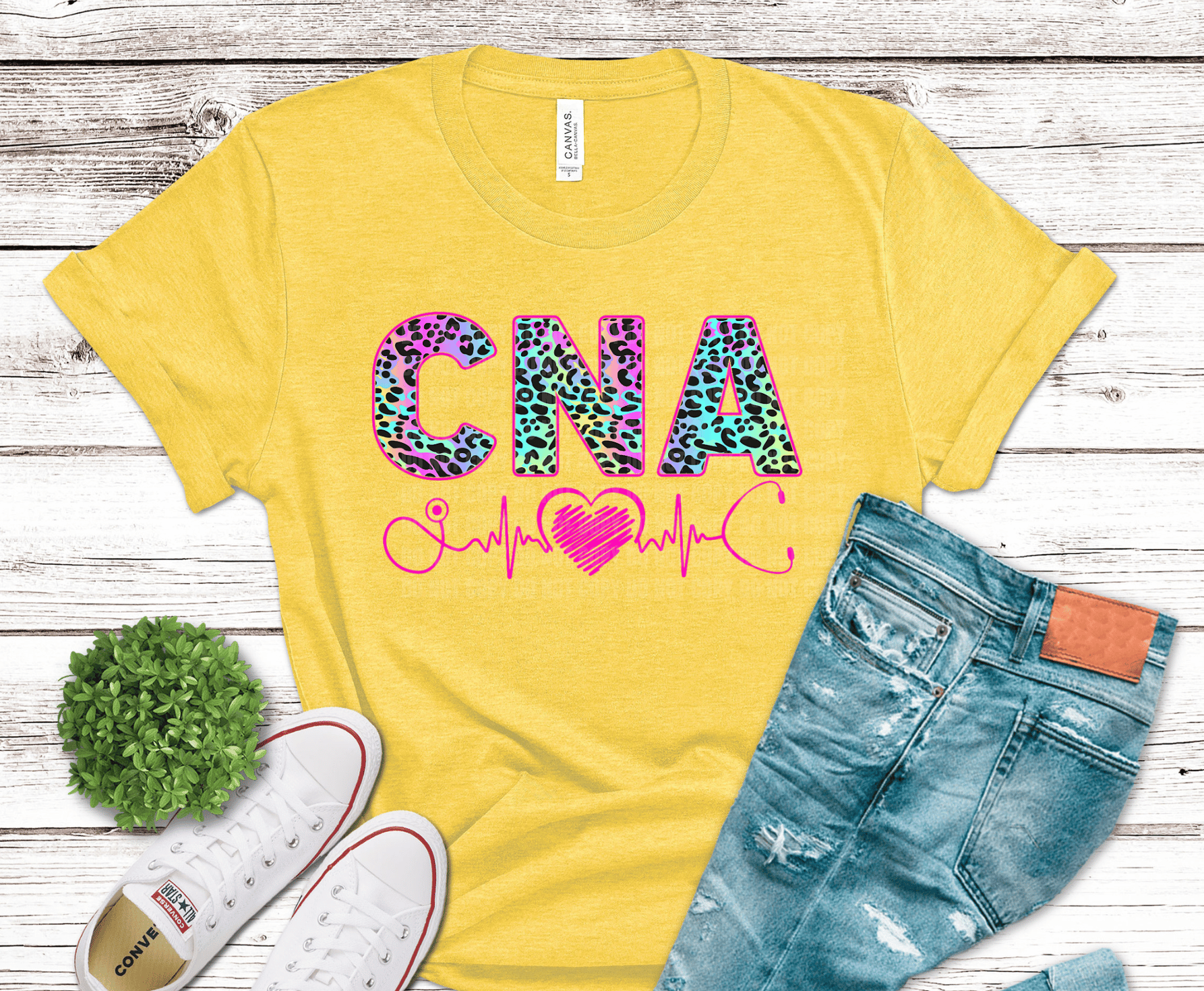 Yellow t-shirt with 'CNA' design on a wooden surface with jeans and sneakers.