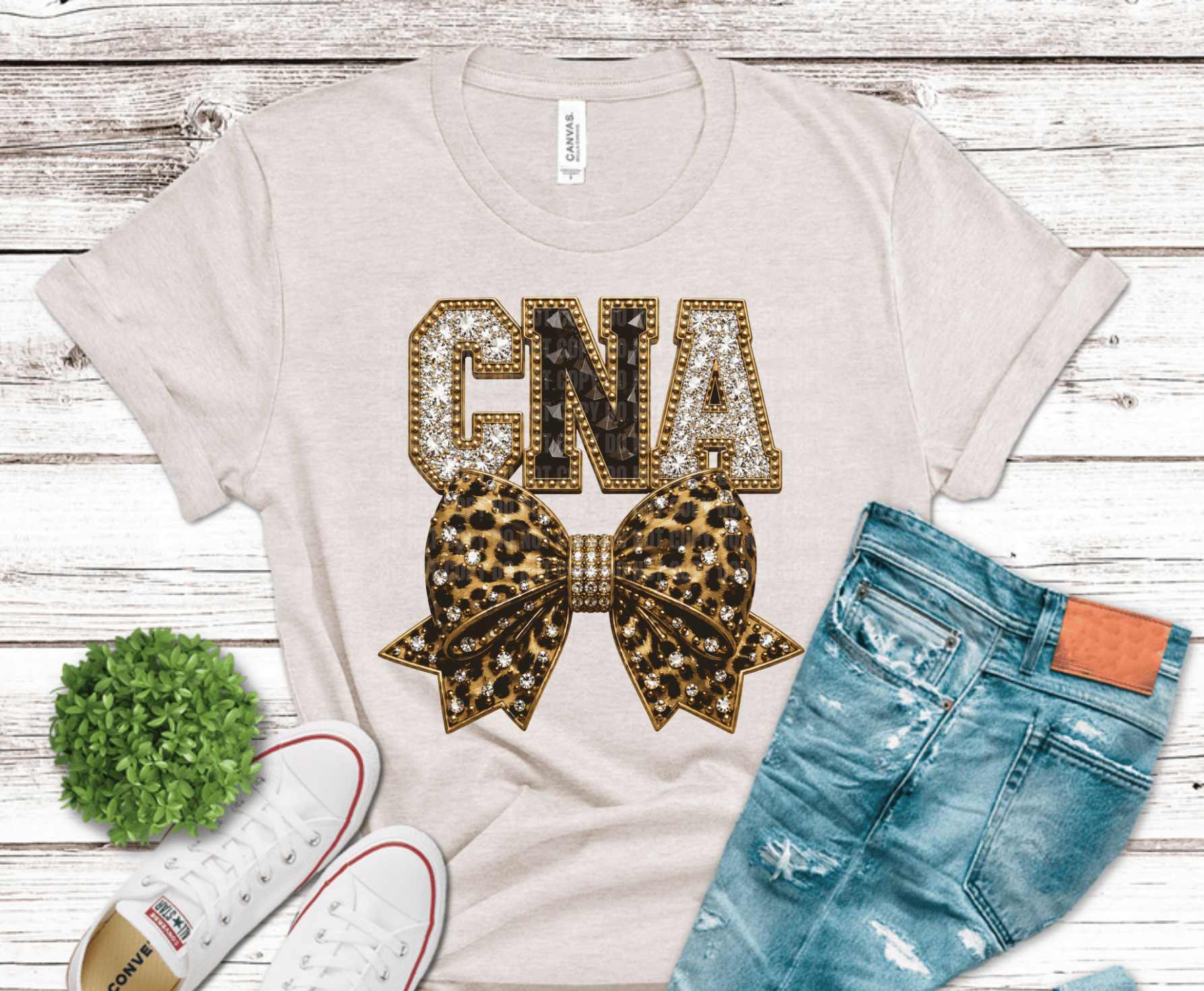 White t-shirt with 'GNA' and bow design, paired with jeans and sneakers on a wooden surface.