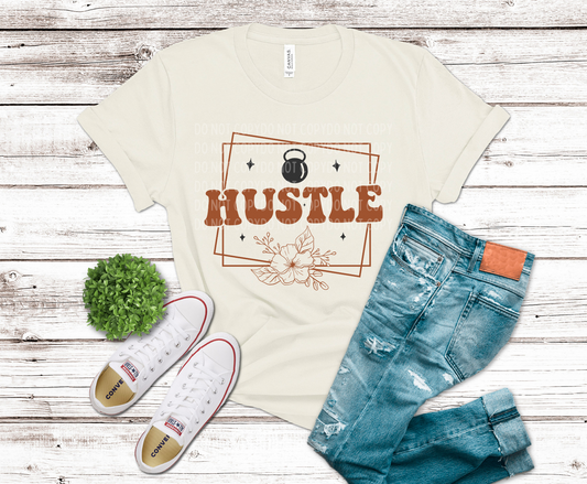 Beige t-shirt with 'HUSTLE' graphic, blue jeans, and white sneakers on a wooden surface