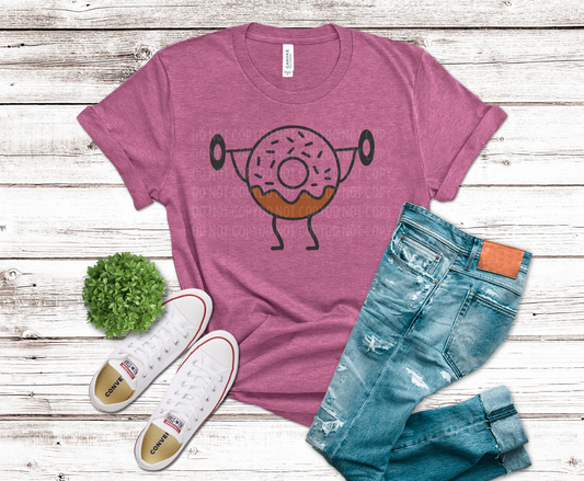 Pink t-shirt with donut graphic, blue jeans, and white sneakers on a wooden surface