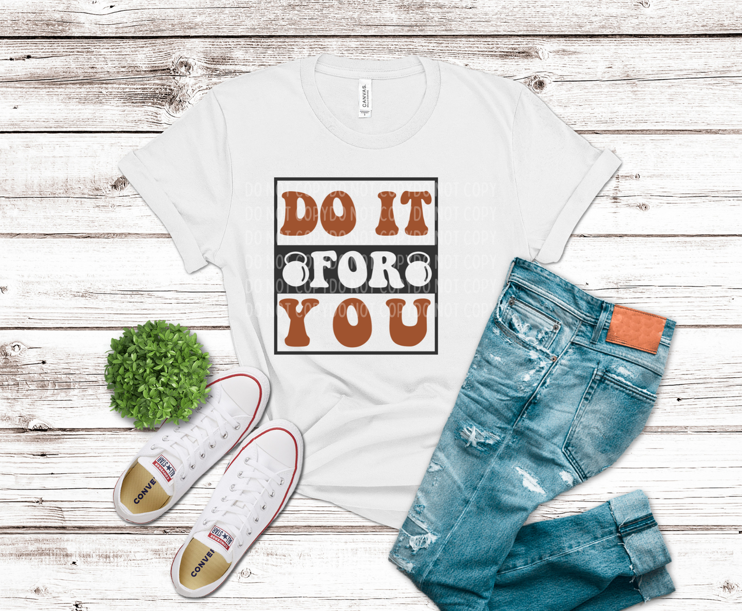 White t-shirt with 'Do It For You' graphic, blue jeans, and white sneakers on a wooden surface.