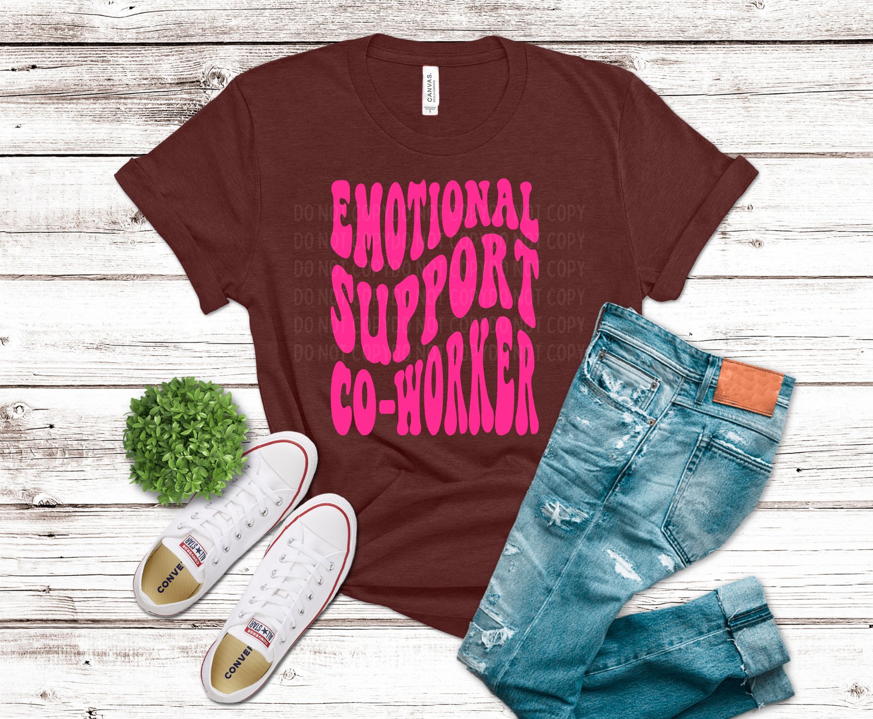 Brown t-shirt with pink text 'EMOTIONAL SUPPORT CO-WORKER', white sneakers, and blue jeans on a wooden surface.