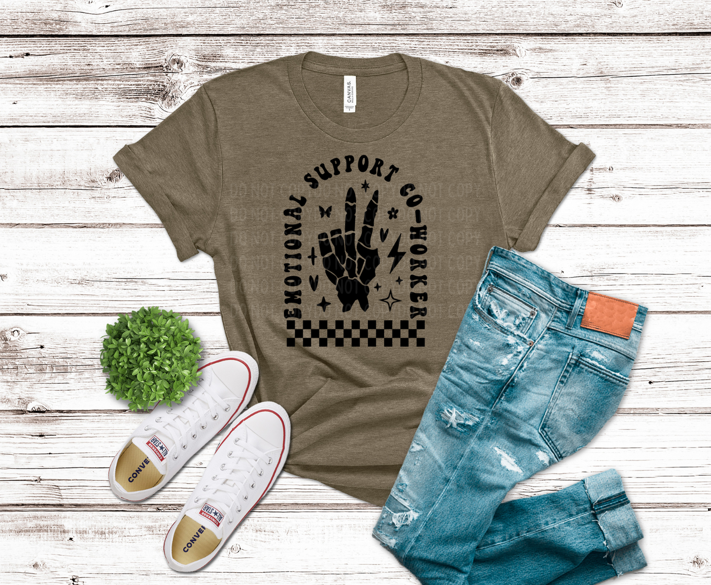 Brown t-shirt with graphic design, blue jeans, white sneakers, and a small plant on a wooden surface.