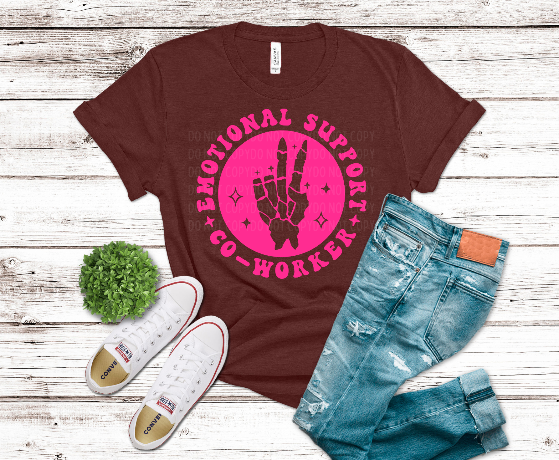 Brown t-shirt with pink graphic and text, paired with jeans and sneakers on a wooden surface.
