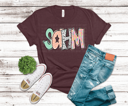 Maroon t-shirt with colorful 'SOHM' design, blue jeans, and white sneakers on a wooden surface.