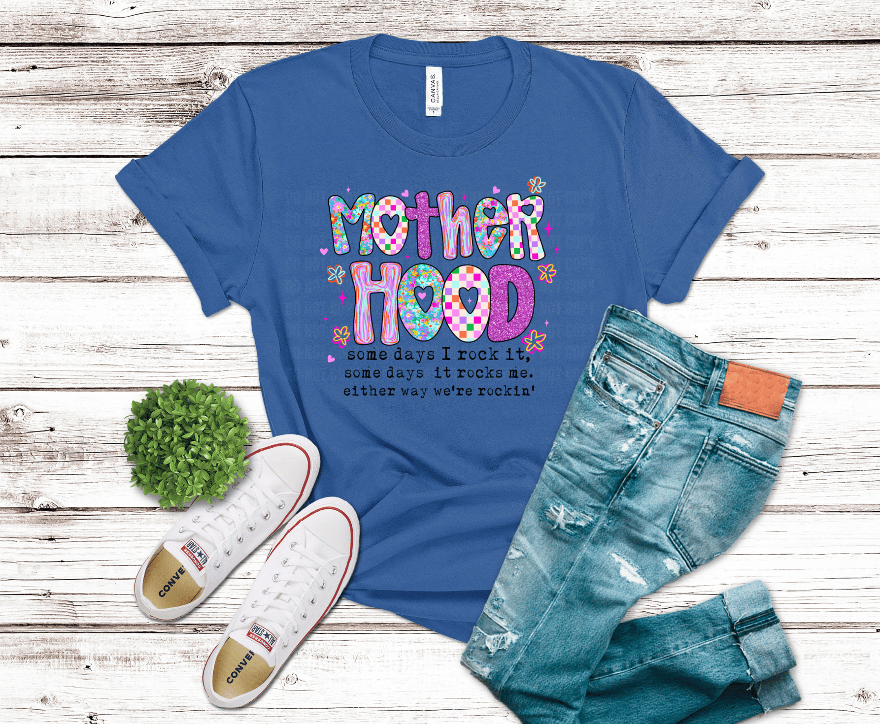 Blue t-shirt with 'Mother Hood' text, white sneakers, and jeans on a wooden surface