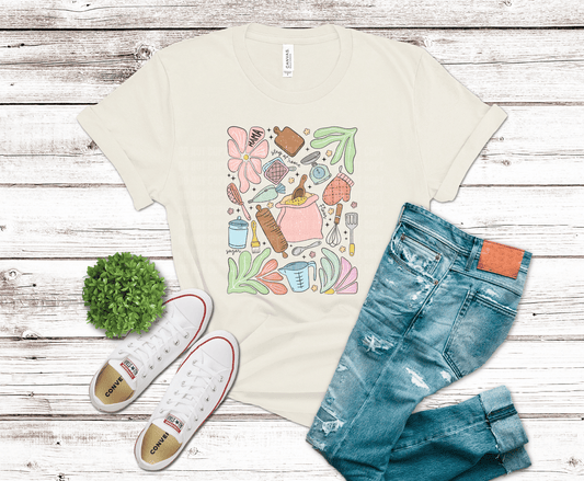 Beige t-shirt with colorful graphic design, blue jeans, and white sneakers on a wooden surface.